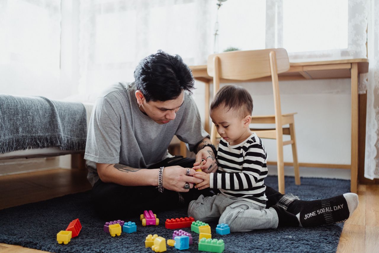 Parent and young child playing with toys together on the living room floor, illustrating parent-implemented strategies in a natural play setting