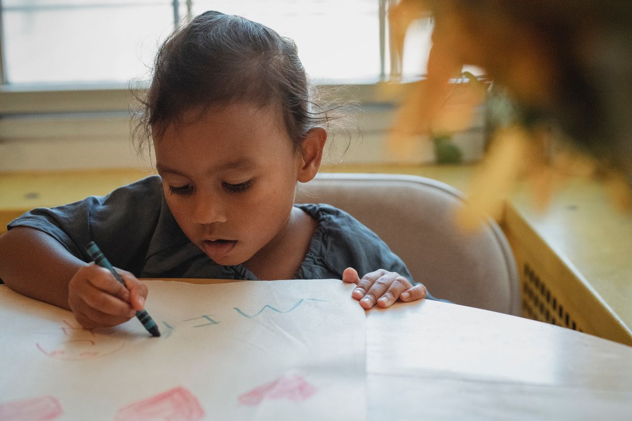 Young child focused on drawing with crayons at a table, building fine motor skills