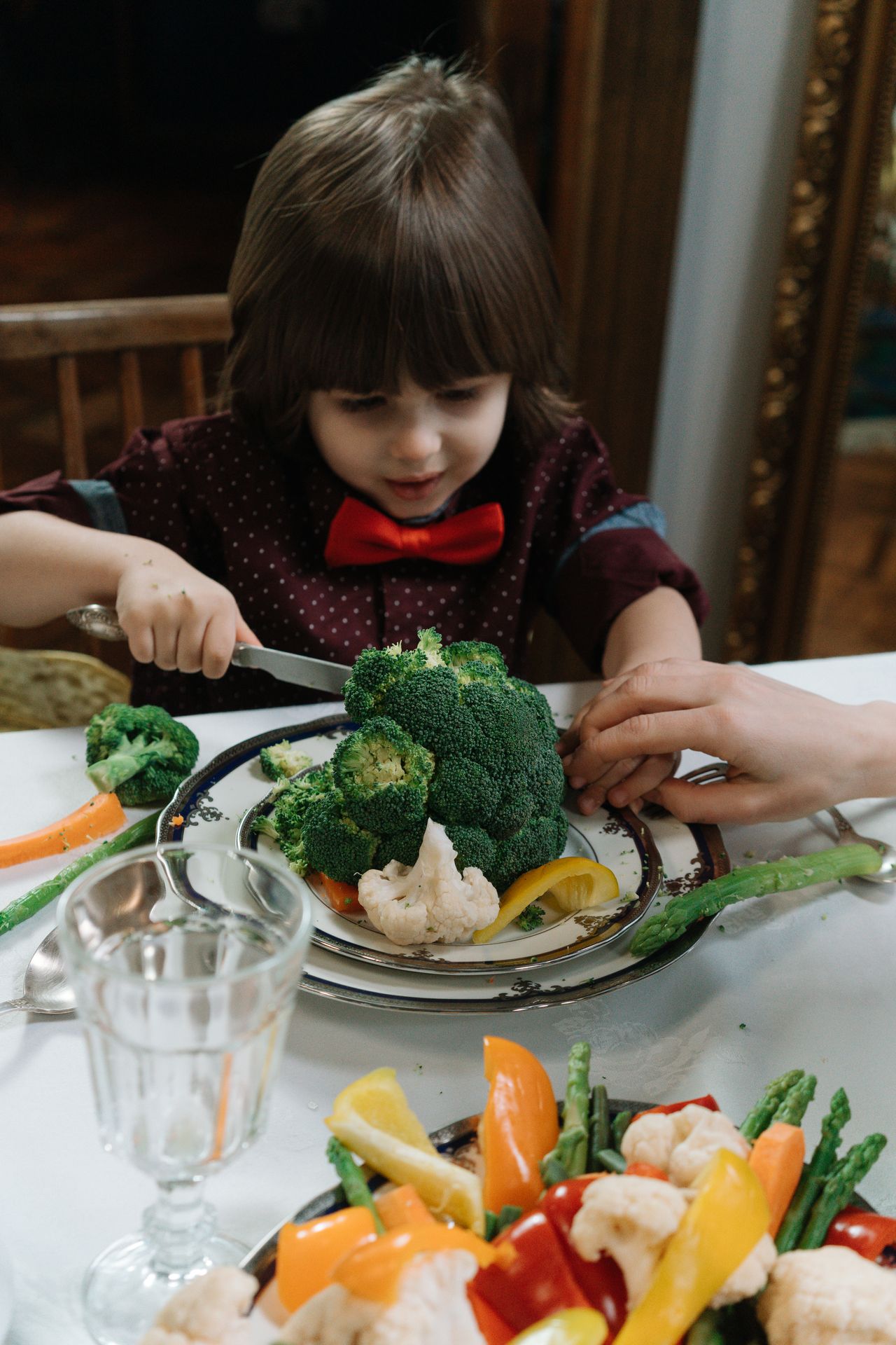 Young child at a table hesitating in front of a plate of colorful vegetables at mealtime